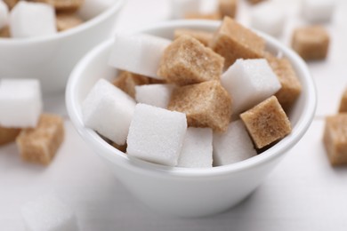 Photo of Different sugar cubes in bowl on white table, closeup