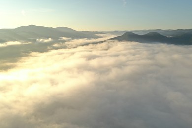 Aerial view of beautiful mountains covered with fluffy clouds on sunny day