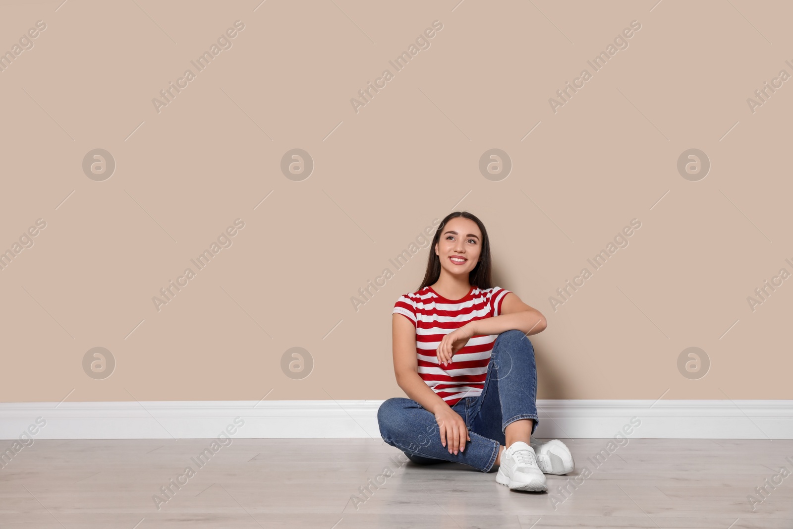 Photo of Young woman sitting on floor near beige wall indoors. Space for text