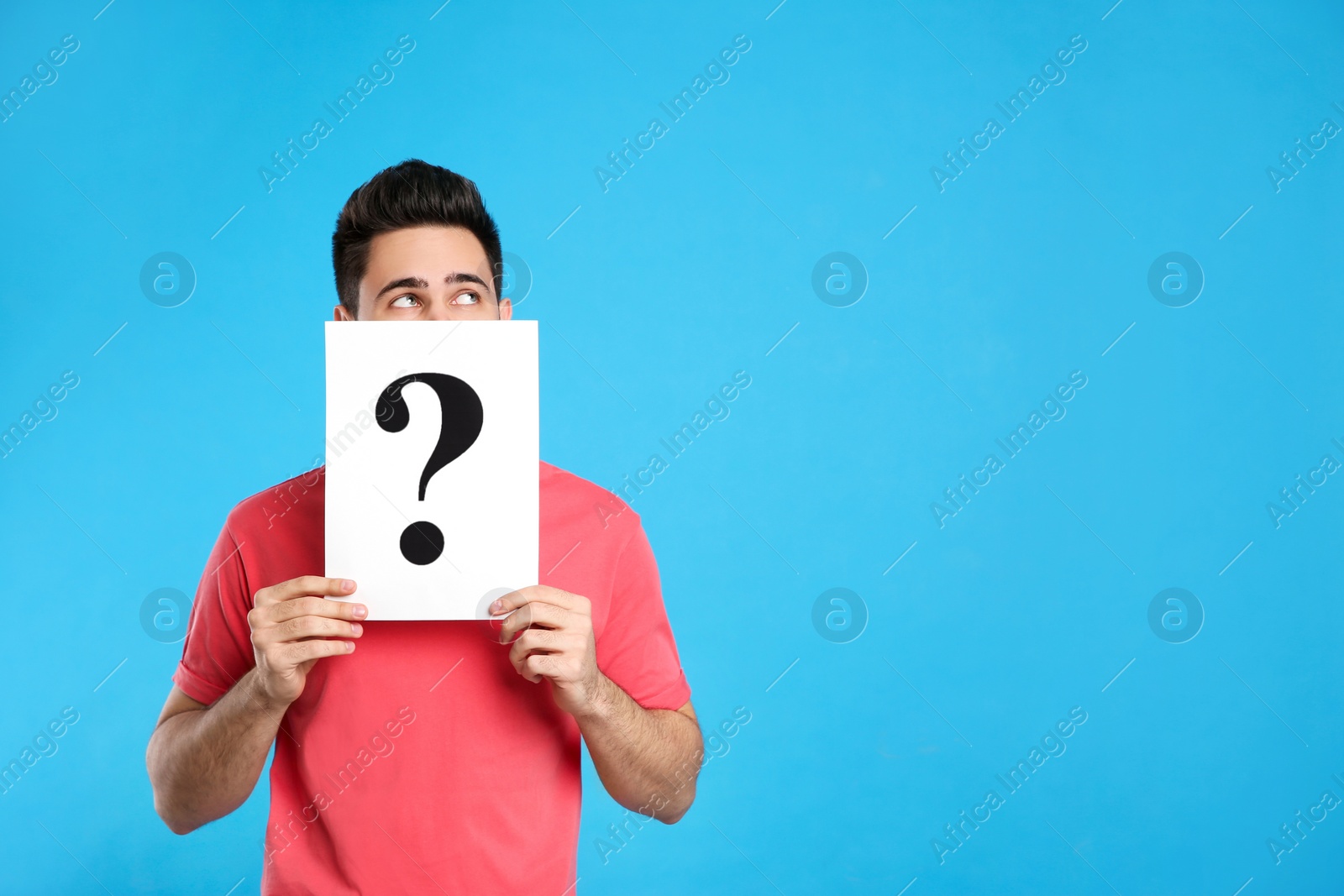 Photo of Young man with question mark sign on light blue background. Space for text