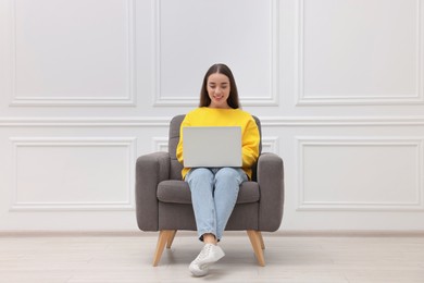 Photo of Beautiful woman with laptop sitting in armchair near white wall indoors