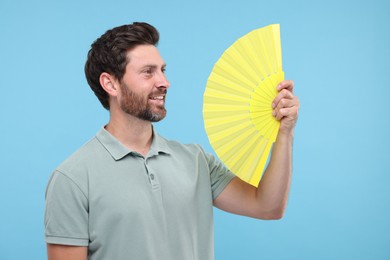 Photo of Happy man holding hand fan on light blue background