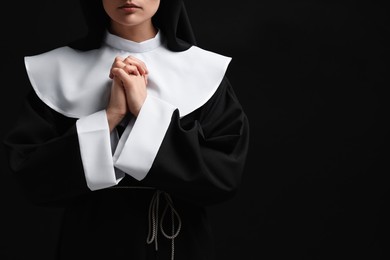 Photo of Nun with clasped hands praying to God on black background, closeup. Space for text