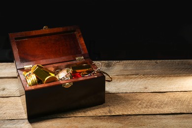Photo of Treasure chest with gold bars, coins, jewelry and gemstones on wooden table. Space for text