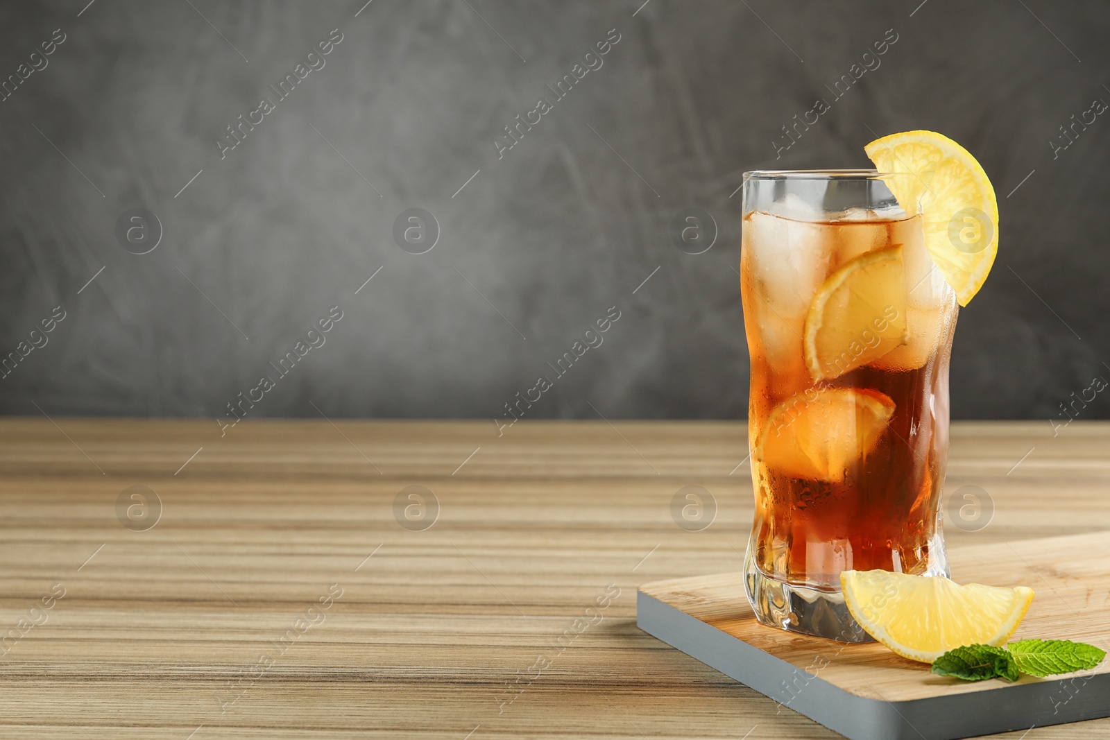 Photo of Glass of tasty ice tea with lemon on wooden table against grey background, space for text