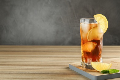 Glass of tasty ice tea with lemon on wooden table against grey background, space for text