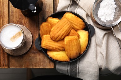 Delicious madeleine cakes, powdered sugar and coffee on wooden table