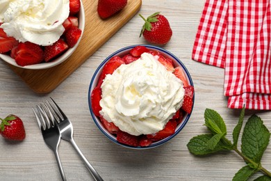Photo of Delicious strawberries with whipped cream served on wooden table, flat lay