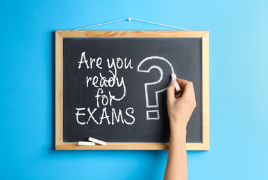 Woman writing phrase ARE YOU READY FOR EXAMS with chalk on blackboard, closeup