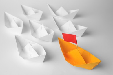 Photo of Group of paper boats following orange one on white background, closeup. Leadership concept