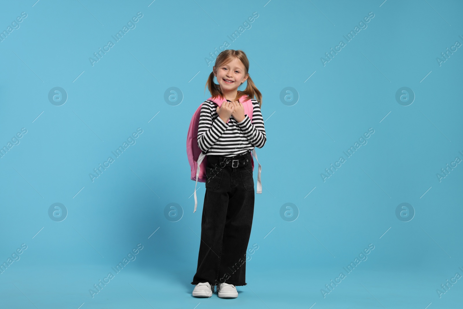 Photo of Happy schoolgirl with backpack on light blue background