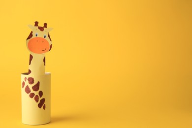 Photo of Toy giraffe made from toilet paper hub on yellow background, space for text. Children's handmade ideas