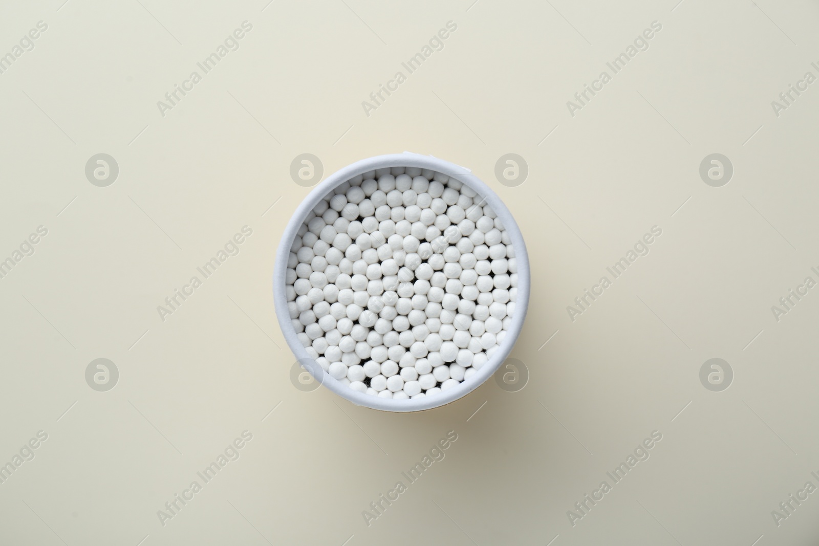 Photo of Container with new cotton buds on beige background, top view