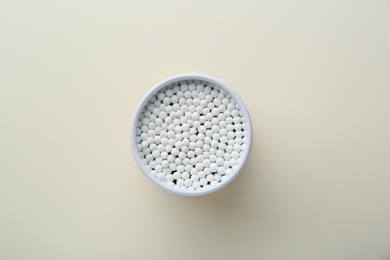 Container with new cotton buds on beige background, top view