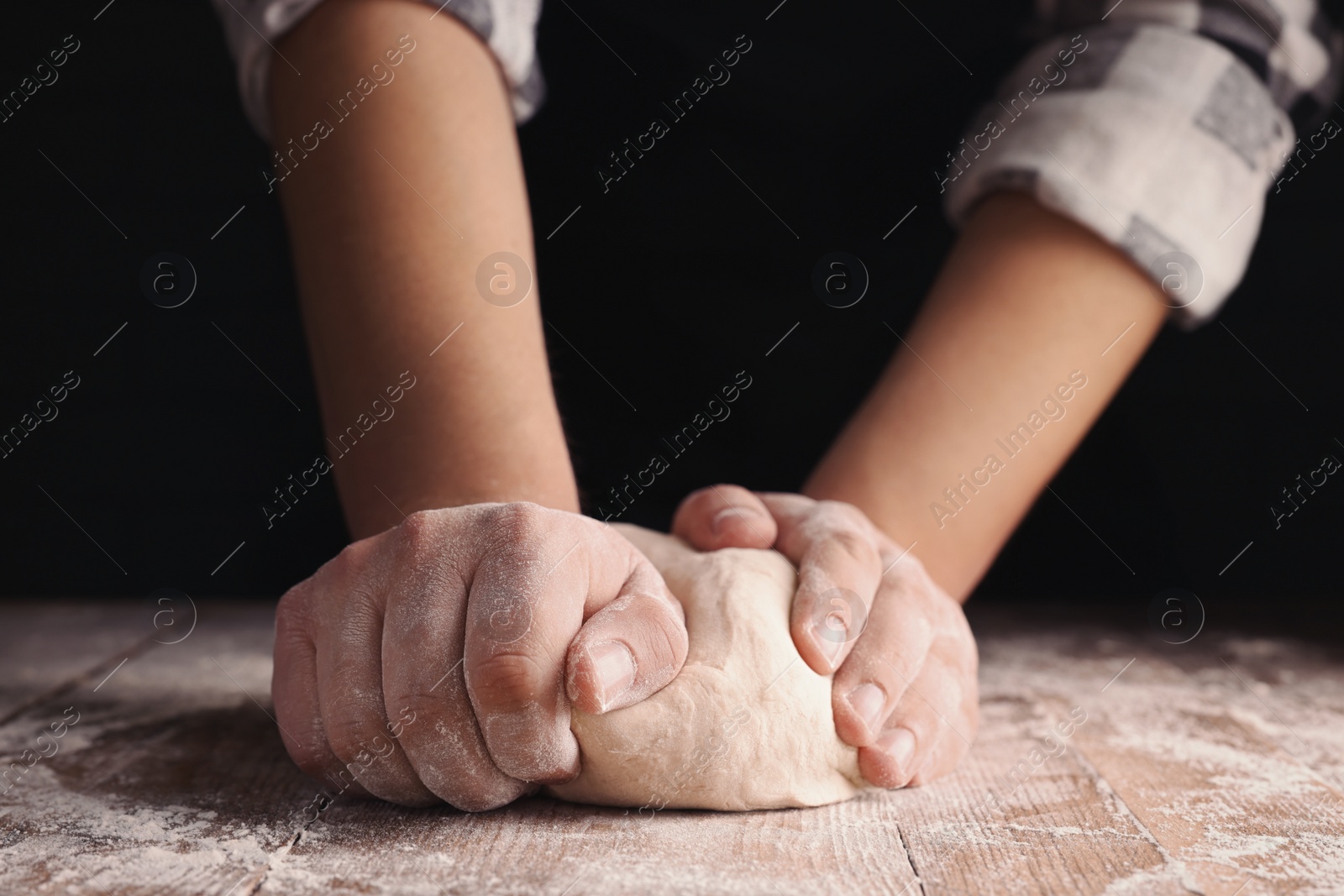 Photo of Man kneading dough at wooden table on dark background, closeup