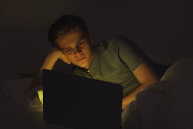Teenage boy using laptop on bed at night. Internet addiction