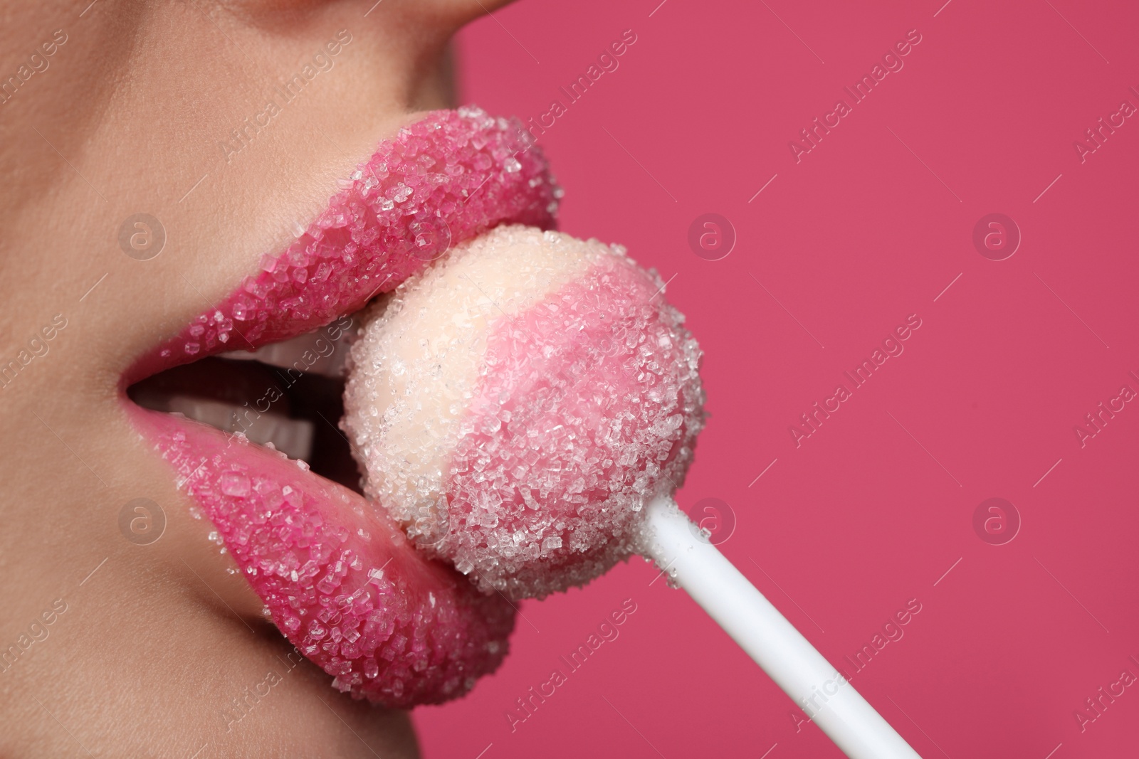 Photo of Young woman with beautiful lips covered in sugar eating lollipop on pink background, closeup