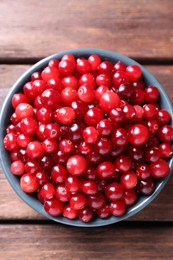 Fresh ripe cranberries in bowl on wooden table, top view