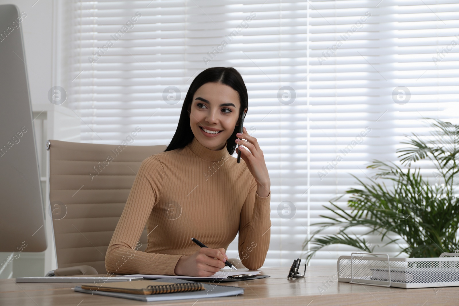 Photo of Secretary talking on smartphone at wooden table in office