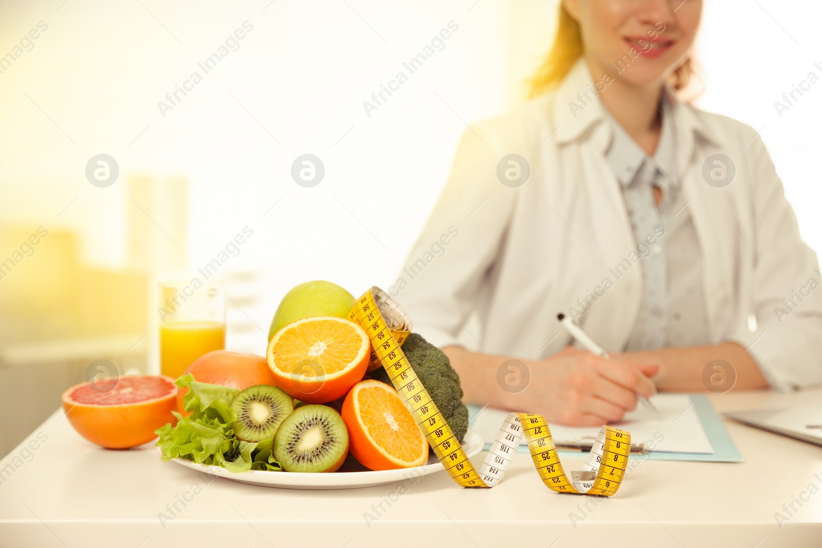 Image of Nutritionist at desk with fruits, vegetables and measuring tape in office, closeup