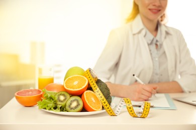 Nutritionist at desk with fruits, vegetables and measuring tape in office, closeup