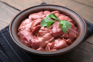 Photo of Bowl with raw chicken liver and parsley on wooden table, closeup