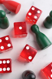 Red dices and game pieces on white marble table, flat lay