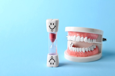 Photo of Dental hourglass and educational model of oral cavity with teeth on color background. Space for text