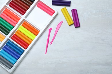 Colorful plasticine and tools on white table, flat lay. Space for text