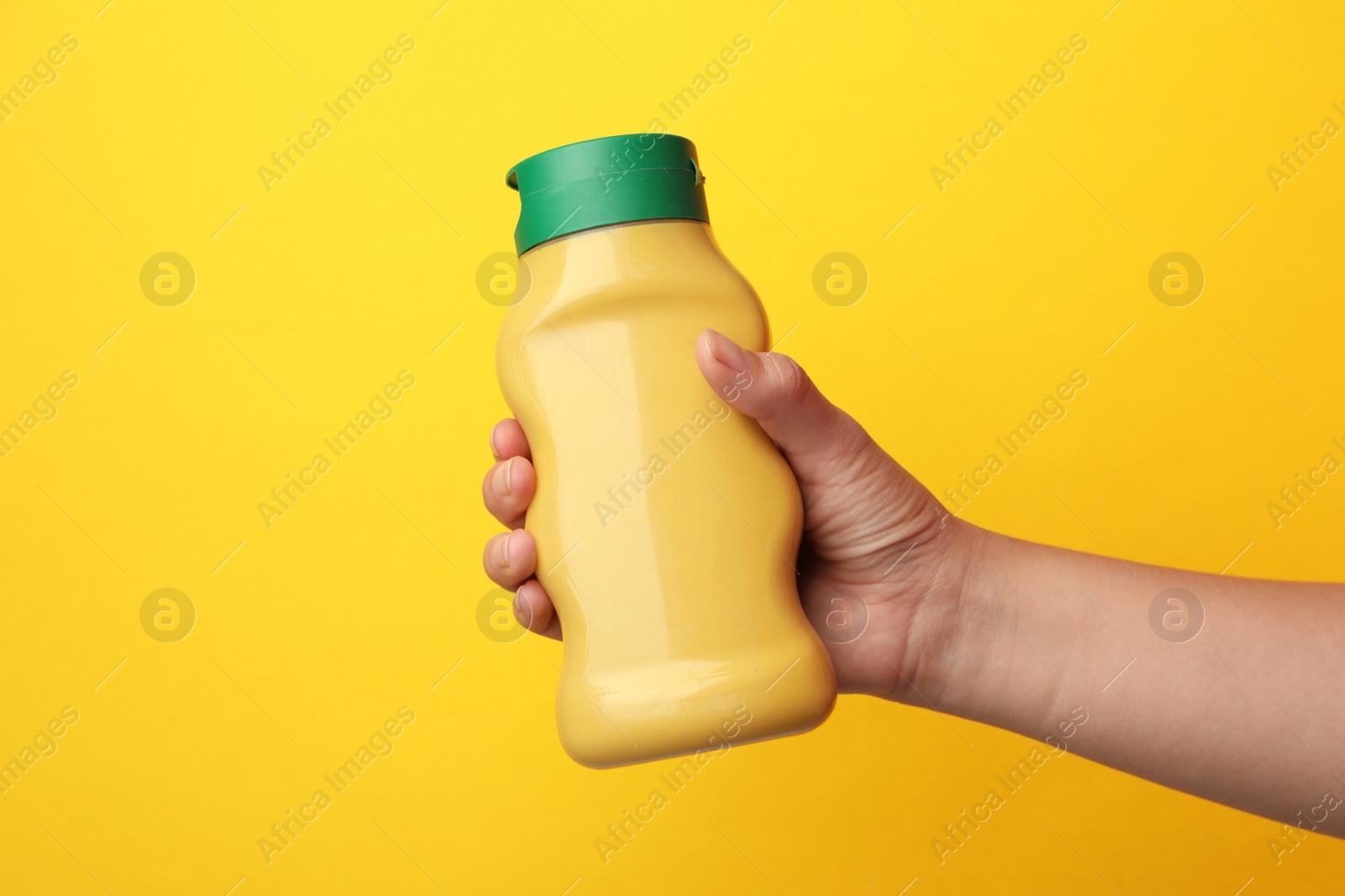 Photo of Woman with bottle of mustard on yellow background, closeup