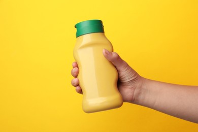 Photo of Woman with bottle of mustard on yellow background, closeup