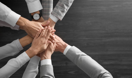 Photo of People holding hands together over grey wooden background, top view. Unity concept