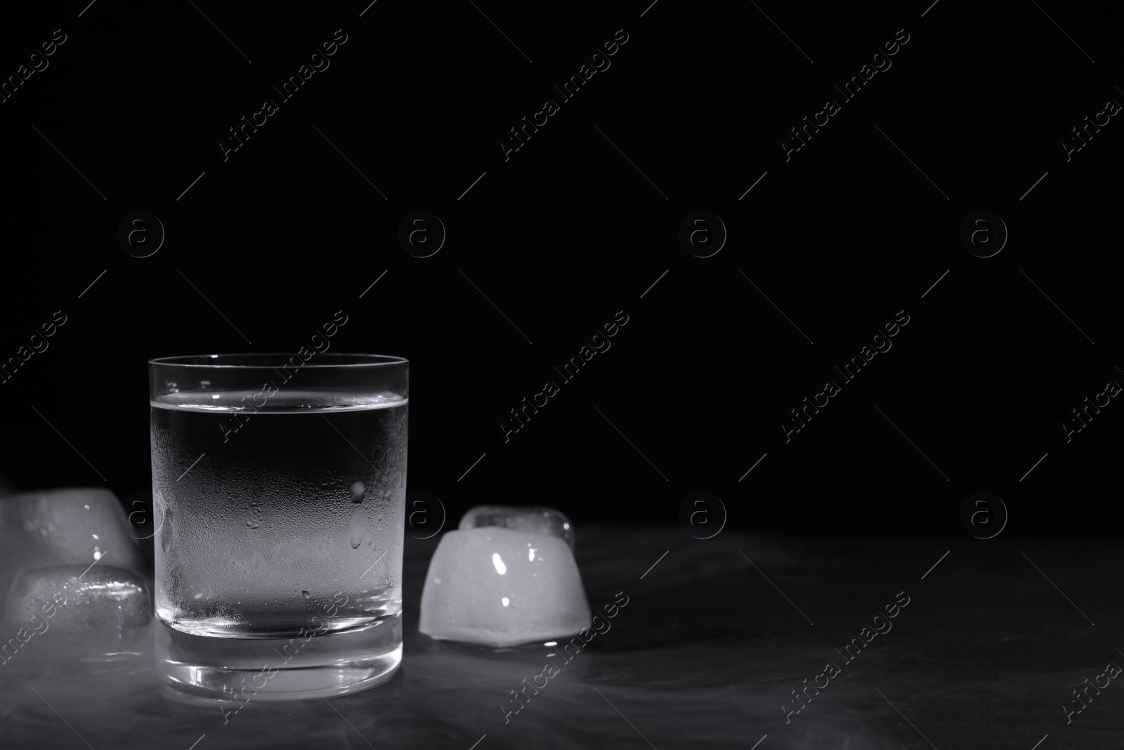 Photo of Vodka in shot glass with ice on table against black background