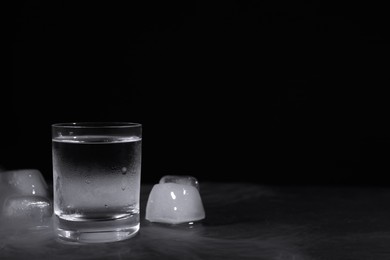 Photo of Vodka in shot glass with ice on table against black background