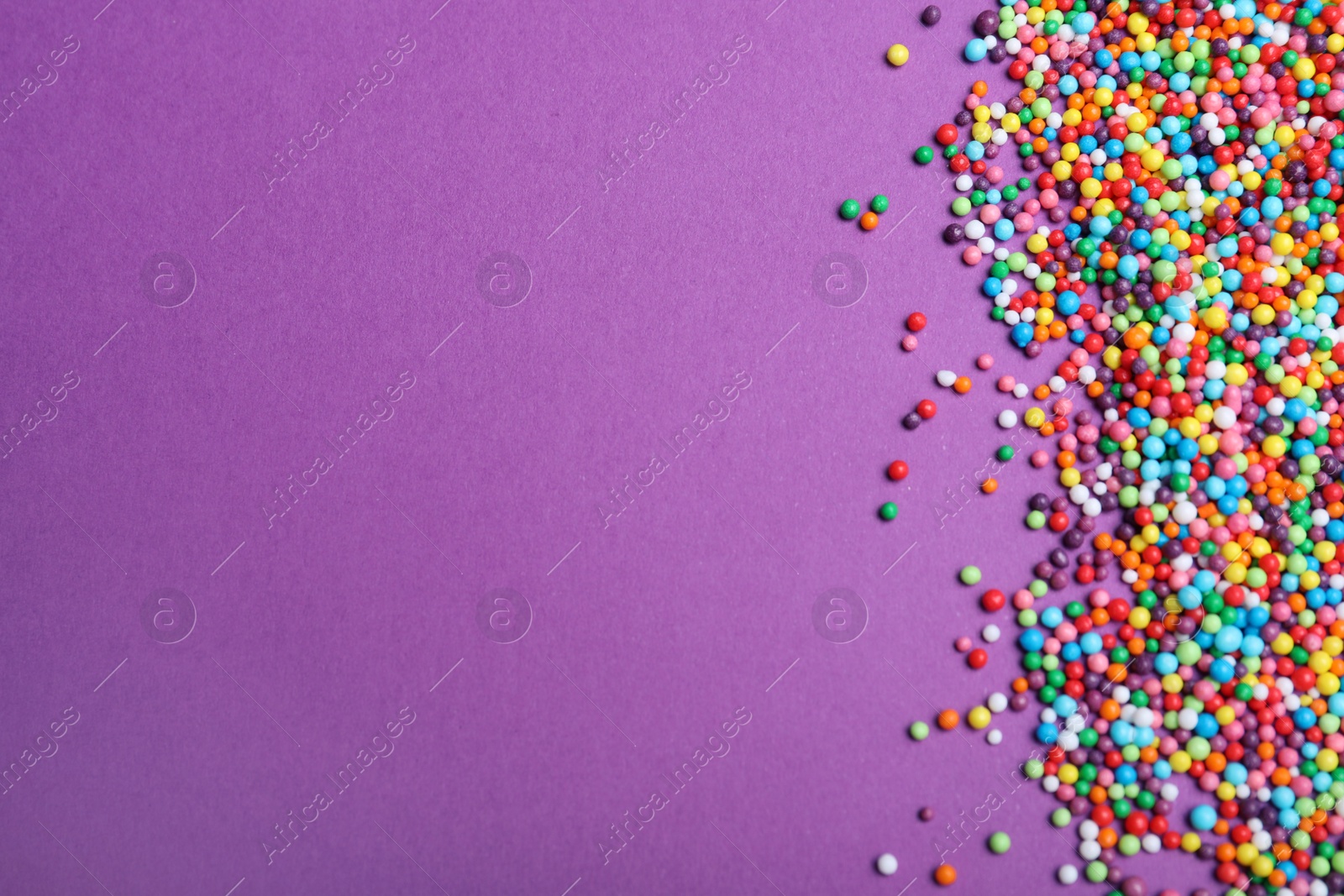 Photo of Colorful sprinkles on purple background, flat lay with space for text. Confectionery decor