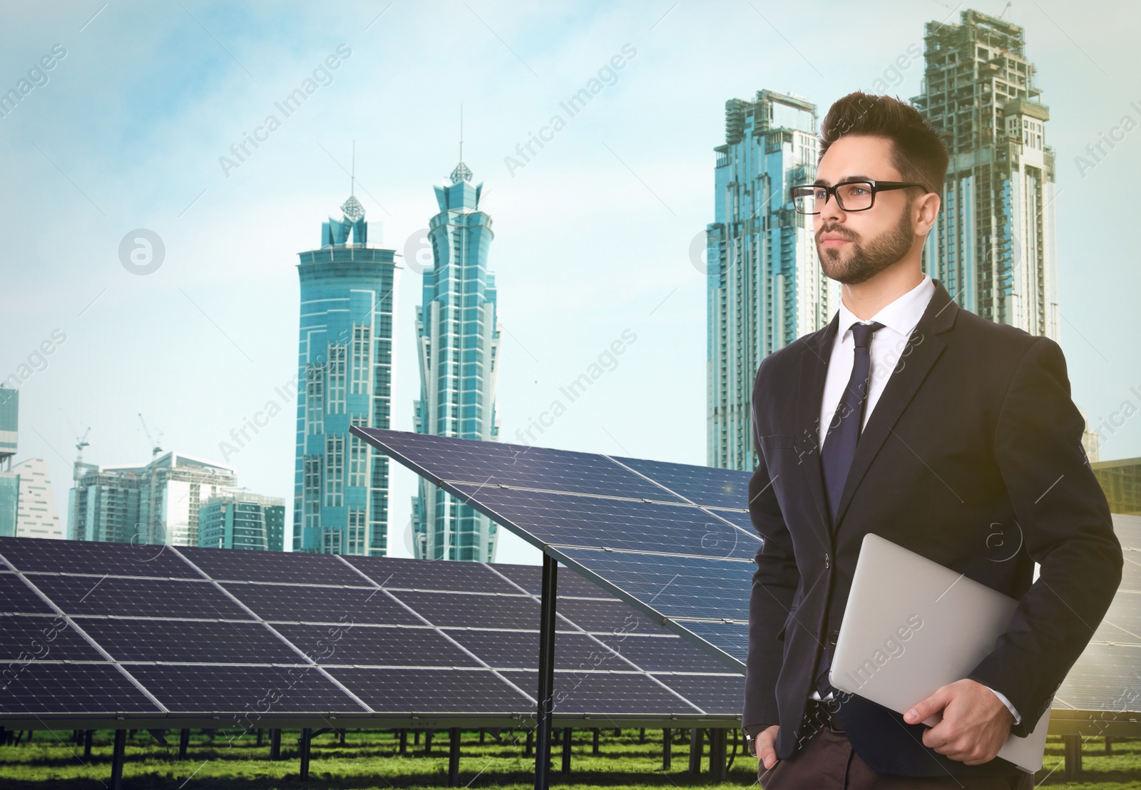 Image of Young businessman with laptop near solar panels and beautiful view of cityscape. Alternative energy source
