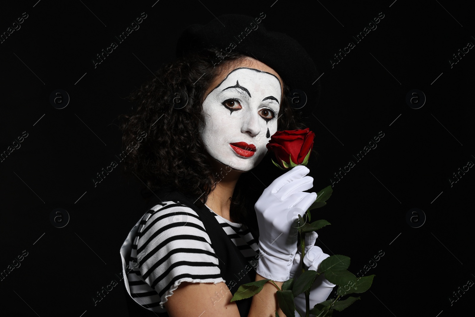 Photo of Young woman in mime costume with red rose posing on black background
