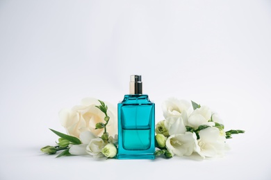 Photo of Bottle of perfume and beautiful flowers on white background