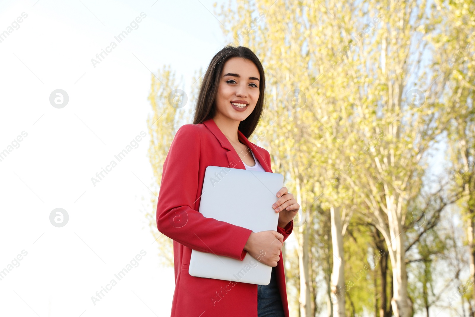 Image of Happy young woman with laptop walking outdoors