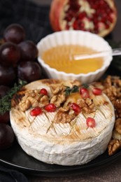 Photo of Plate with tasty baked camembert, honey, walnuts and pomegranate seeds on table, closeup