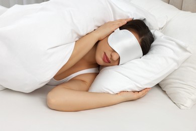 Photo of Unhappy young woman with sleeping mask covering ears in bed