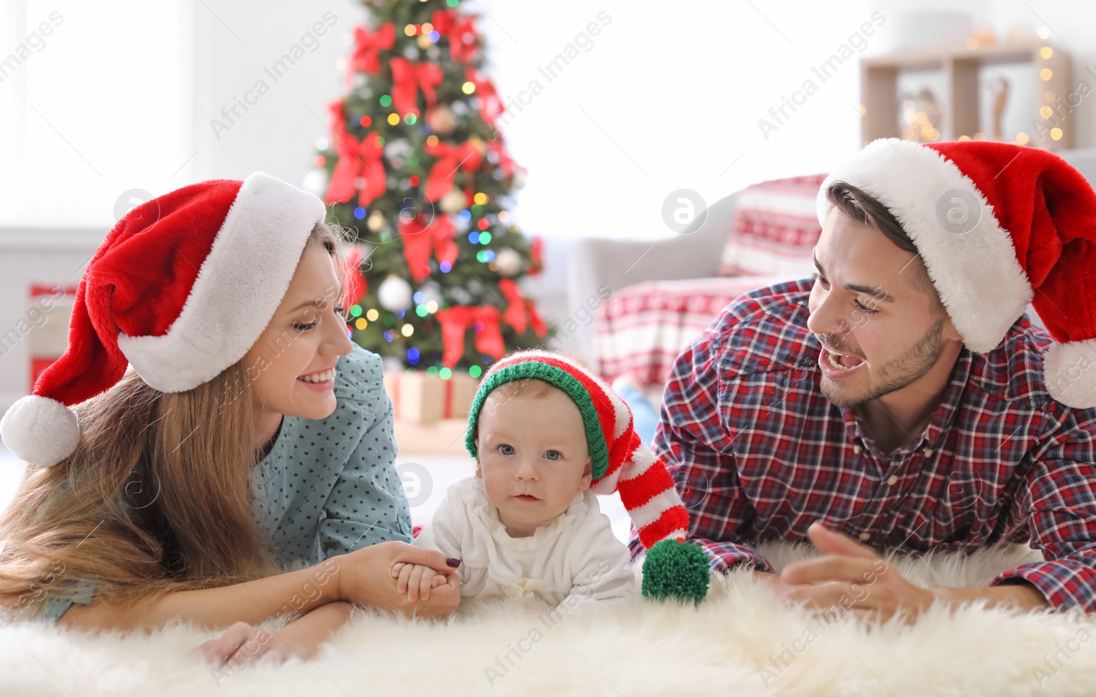 Photo of Happy couple with baby in Christmas hats at home