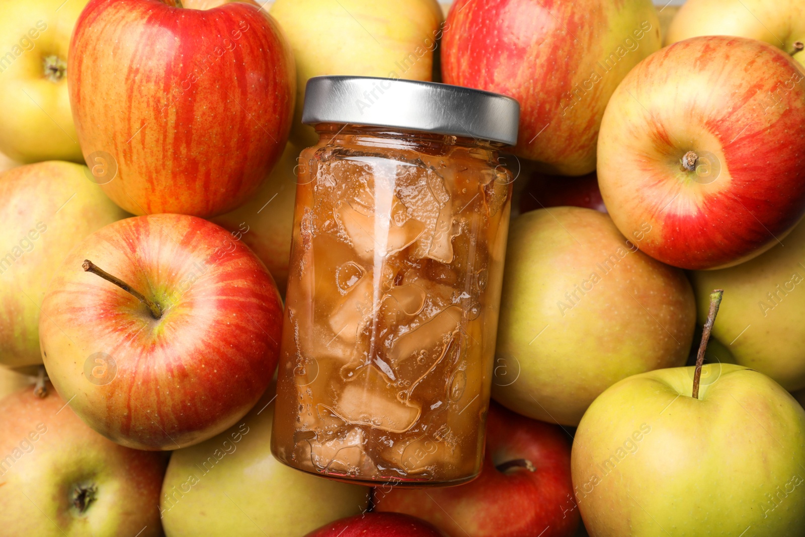 Photo of Delicious apple jam in jar on fresh fruits, top view