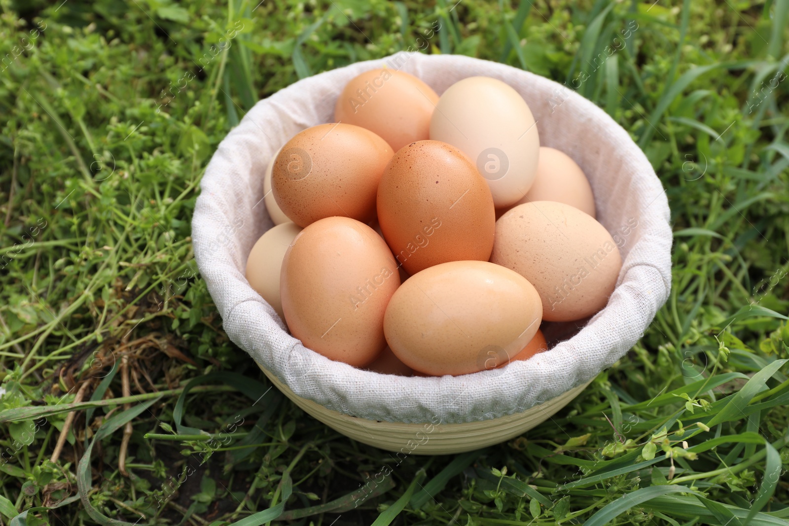 Photo of Fresh chicken eggs in basket on green grass outdoors