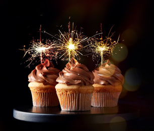 Birthday cupcakes with sparklers on stand against dark background