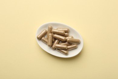 Photo of Vitamin capsules on pale yellow background, top view