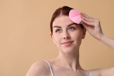 Washing face. Young woman with cleansing brush on beige background, space for text