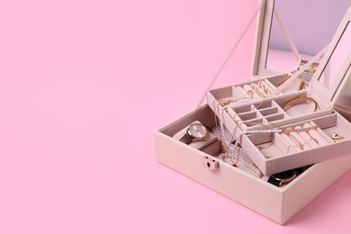 Jewelry box with many different accessories on pink background. Space for text