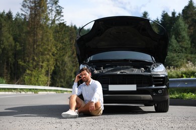 Stressed man sitting on asphalt road near broken car outdoors