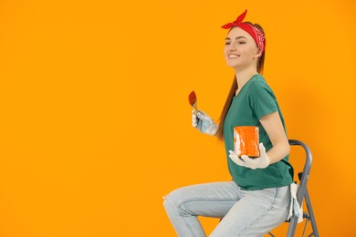 Photo of Happy designer with painting equipment sitting on folding ladder near freshly painted orange wall, space for text